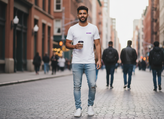 Man walking on a city street holding a coffee cup, wearing a white t-shirt with the Ironic logo on the chest.