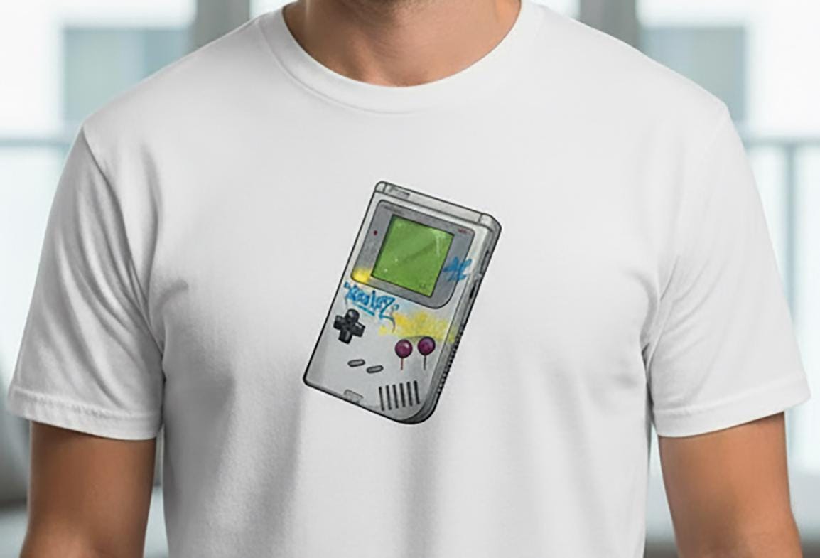 White t-shirt with a graphic of a handheld gaming device on a blurred indoor background