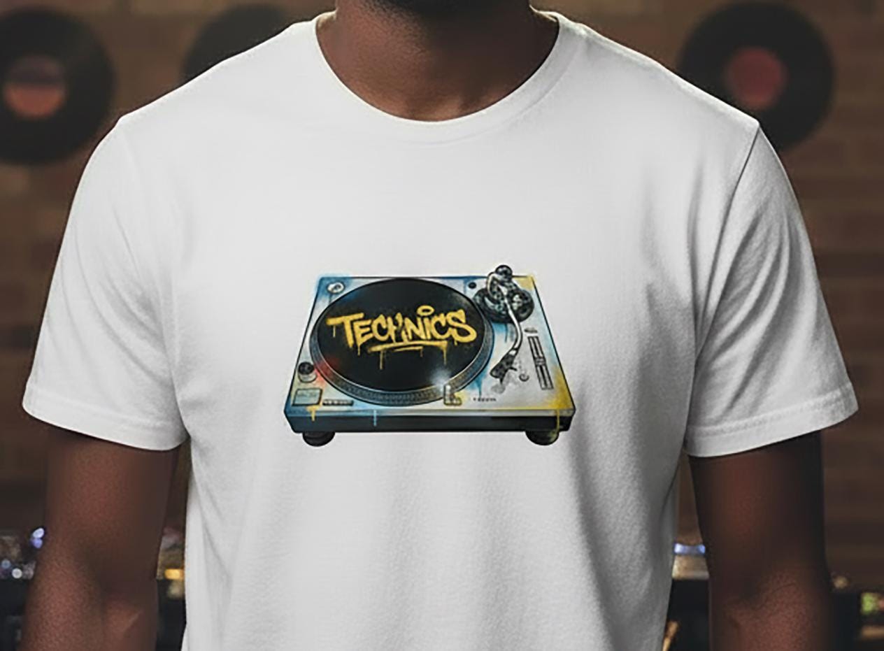 White t-shirt with Technics turntable graffiti graphic worn by a person, with vinyl records in the background.