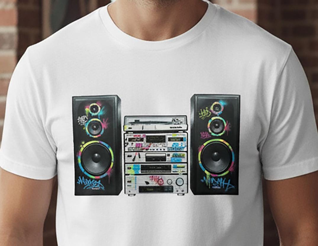 White t-shirt with a colorful graphic of a Hi-Fi system and speakers on a brick wall background.
