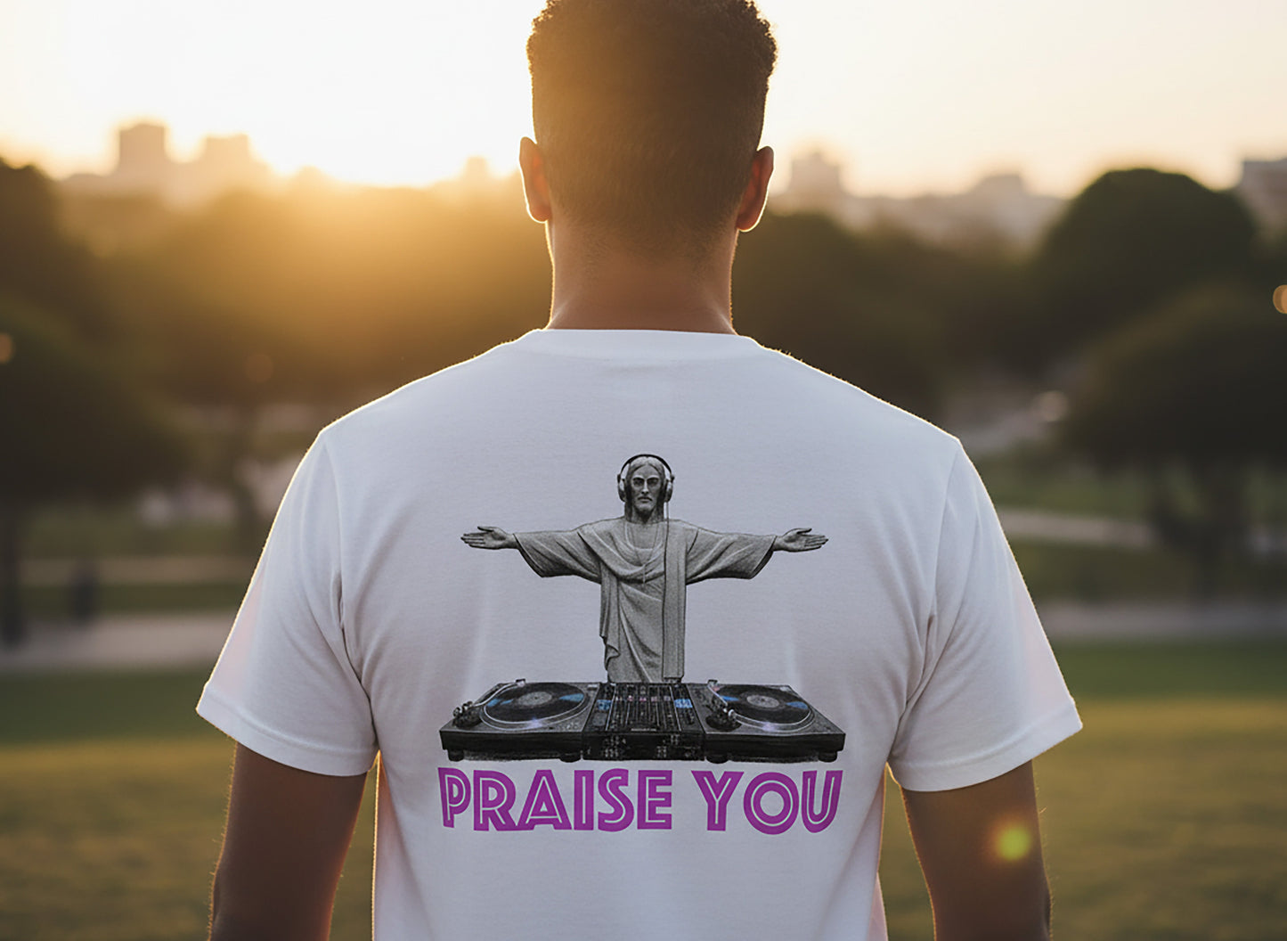 Person wearing a white t-shirt with a graphic design of a statue at DJ decks and text saying Praise You, standing in a park at sunset.